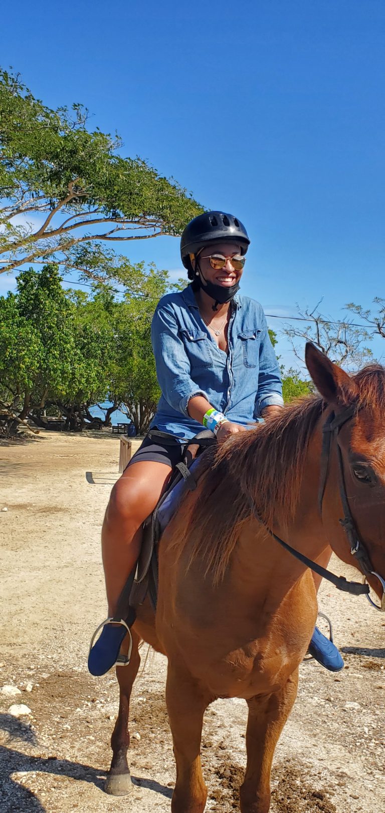 Black woman with a helmet on riding a horse in montego bay Jamaica