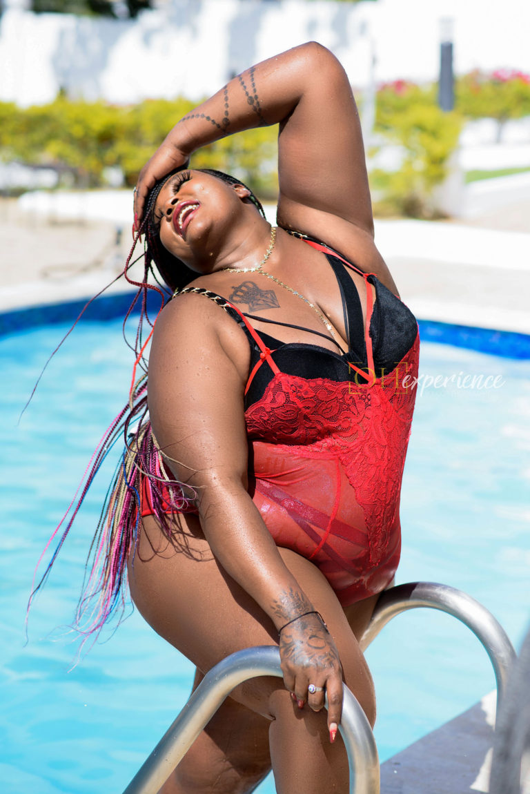 BLACK WOMAN IN RED AND BLACK LINGERIE IN A POOL. hER HAND IS ON HER HEAD