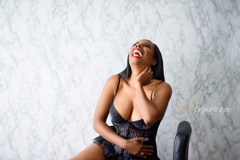 Laughing black woman in black sparkle lingerie sitting on chair
