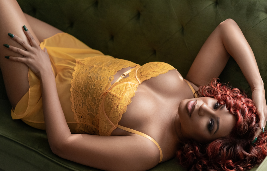 BLACK WOMEN WITH BRIGHT RED HAIR LAYING ON GREEN SOFA IN BRIGHT YELLOW LINGERIE