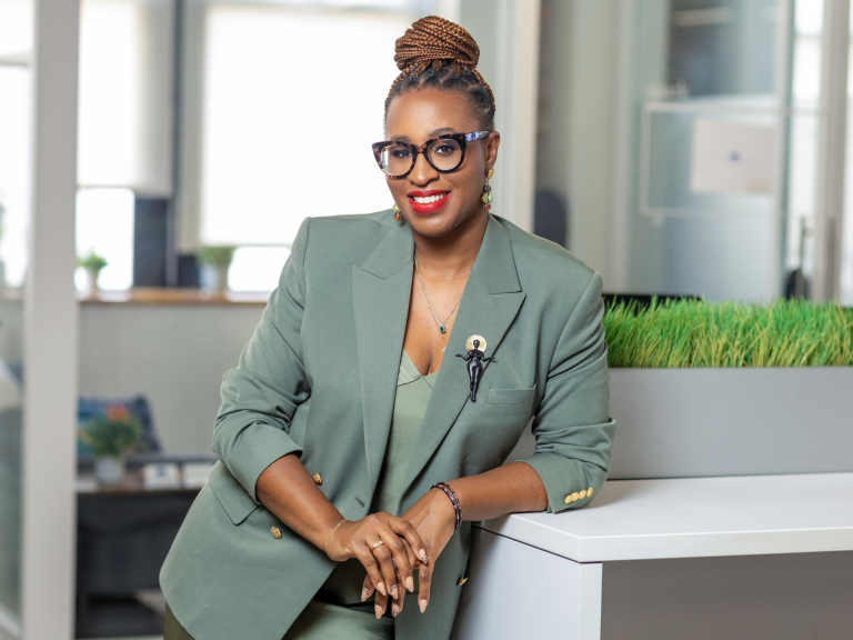Black woman in a green silk dress and green matching blazer smiling